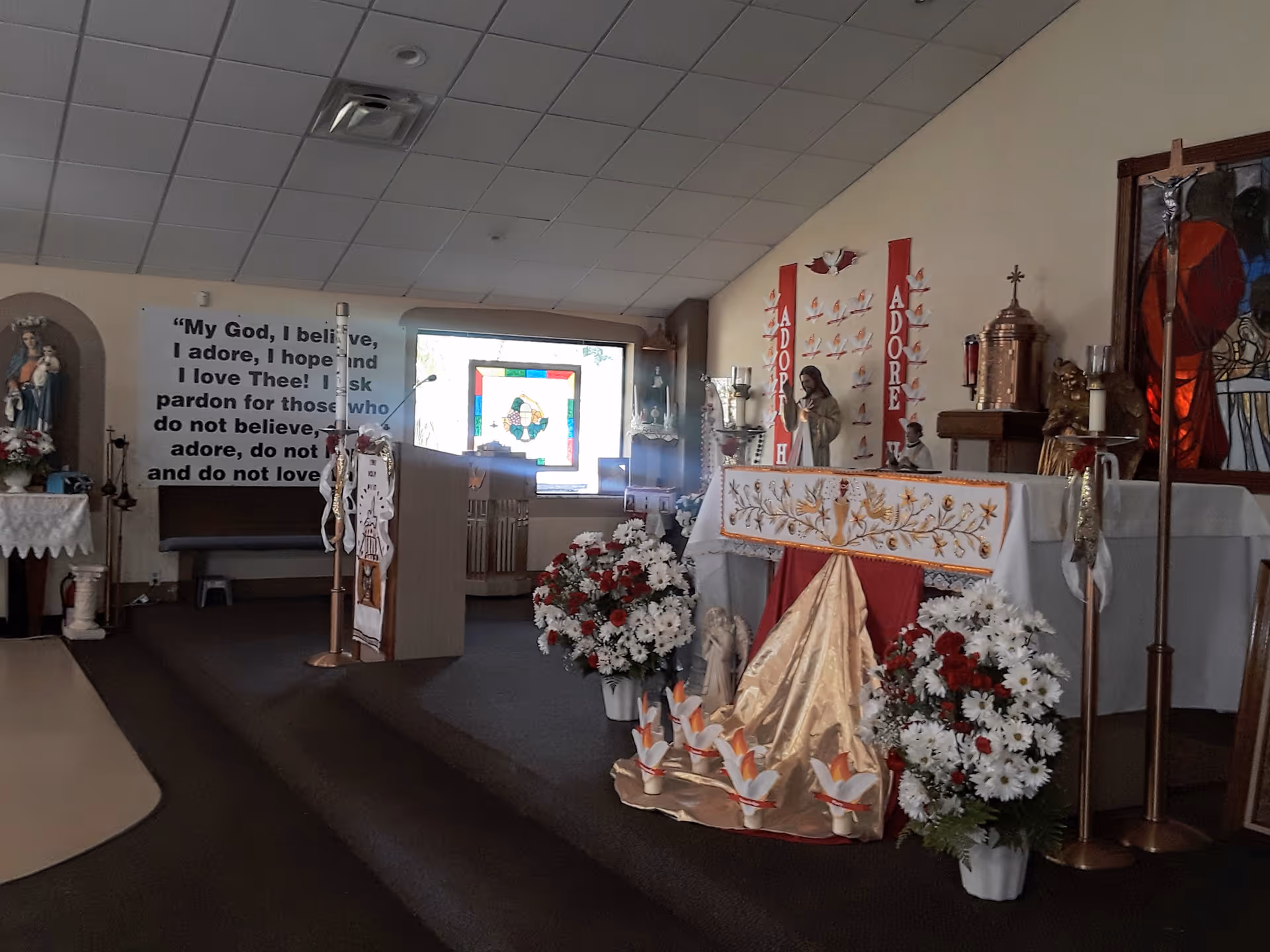 Interior chapel with altar, flowers, statues, and stained glass window.
