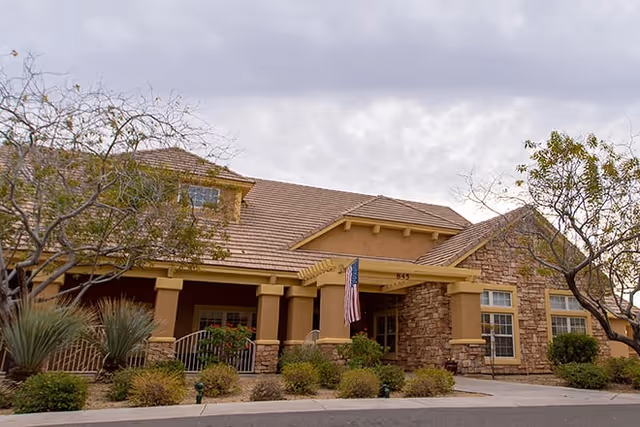 Front exterior of Brookdale North Gilbert showing entrance, pillars, flag, and landscaped shrubs.