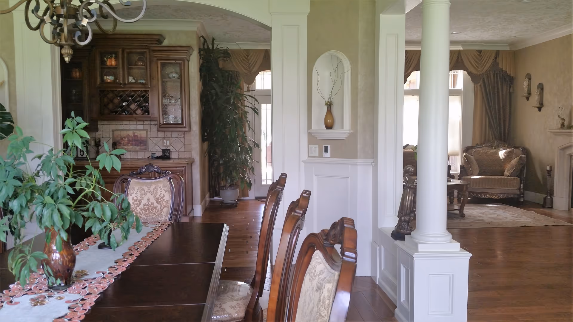 Open-concept dining area with a wooden table, ornate chairs, chandelier, and adjacent living room.