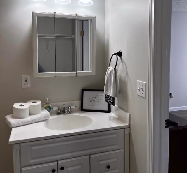 Bathroom vanity with sink, mirror cabinet, towels, and a small framed sign.