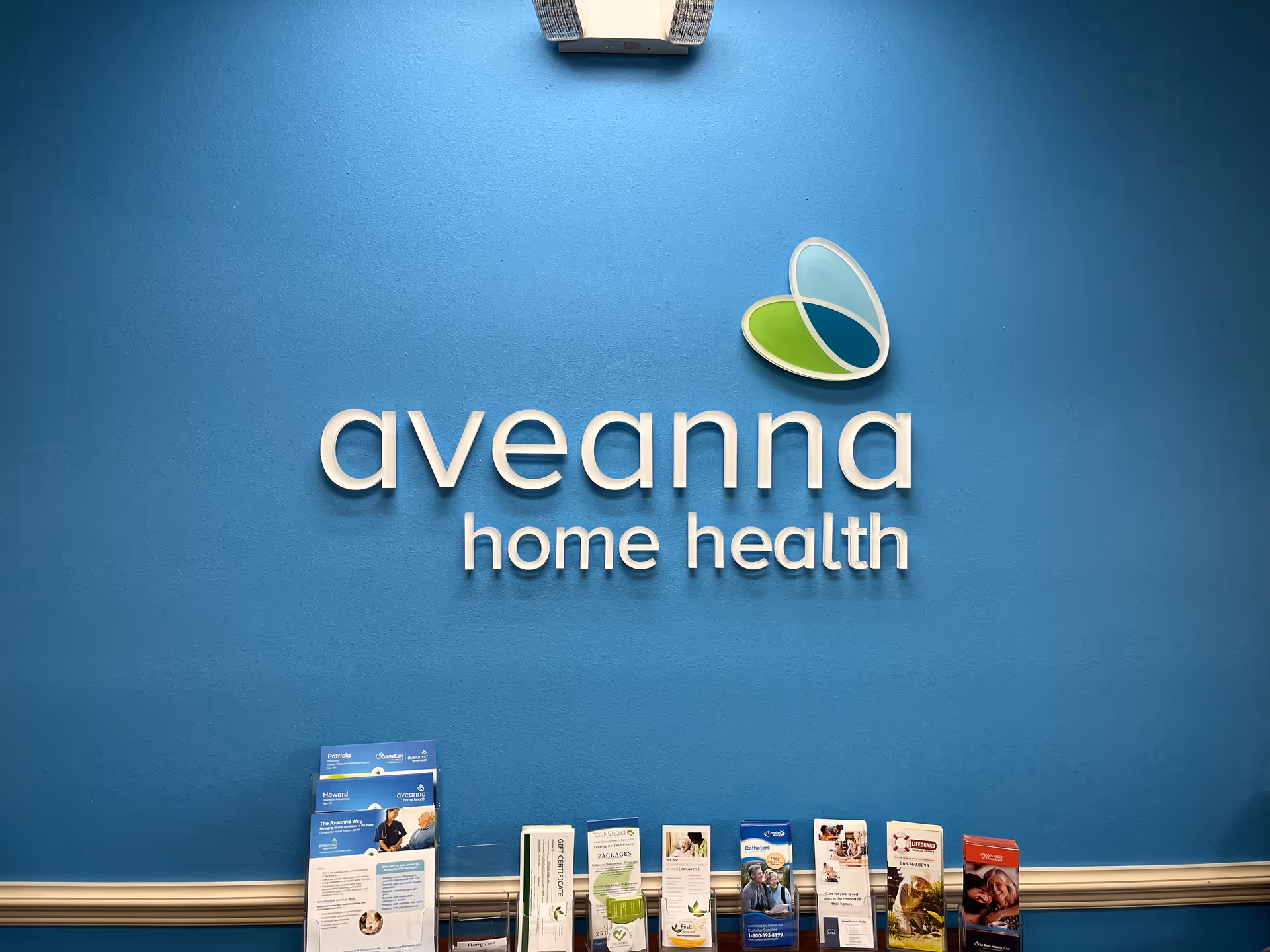Blue interior wall with Aveanna Home Health sign and brochures on a ledge.