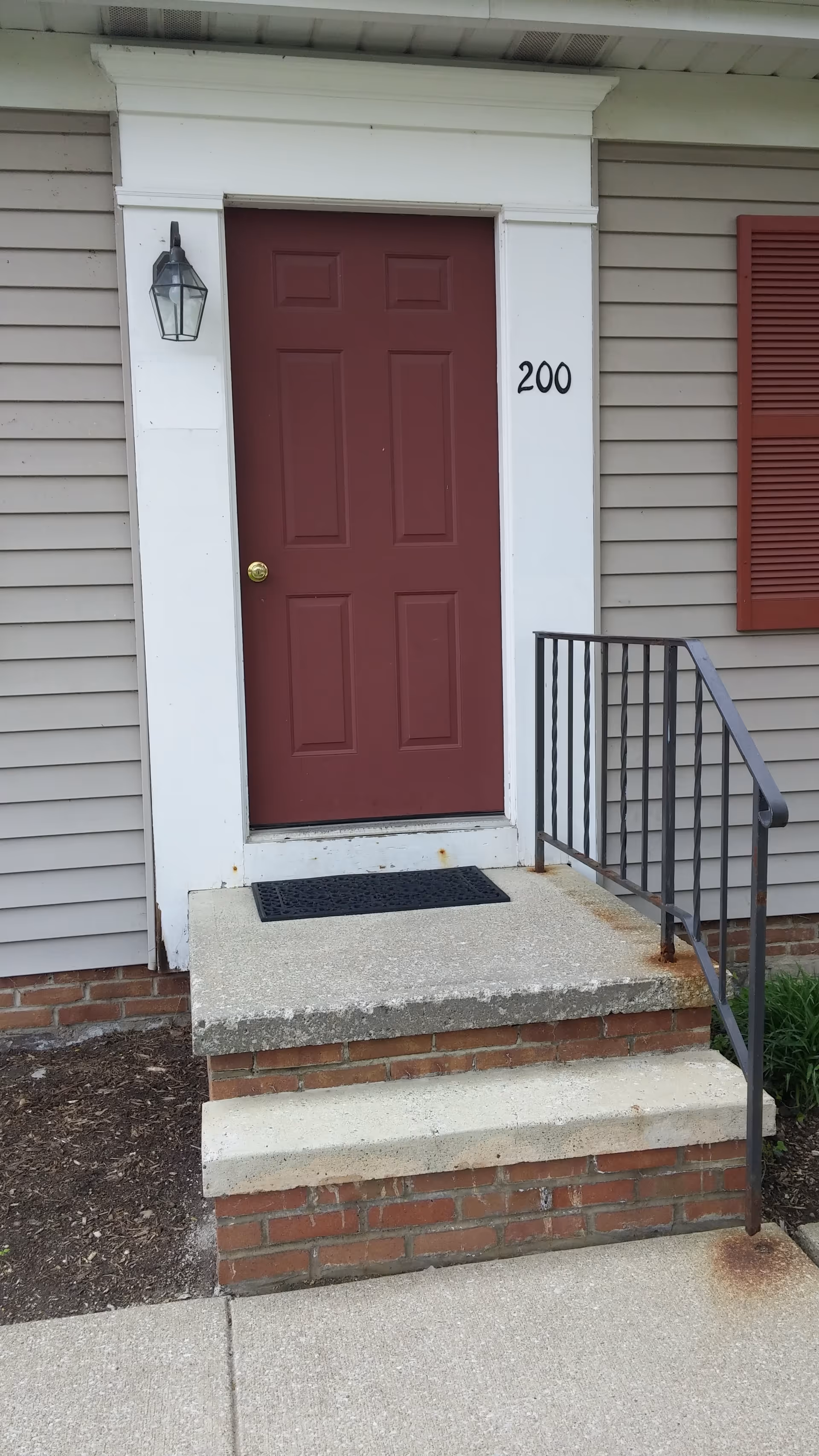 Red front door with white trim and steps, number 200, at a residential entrance