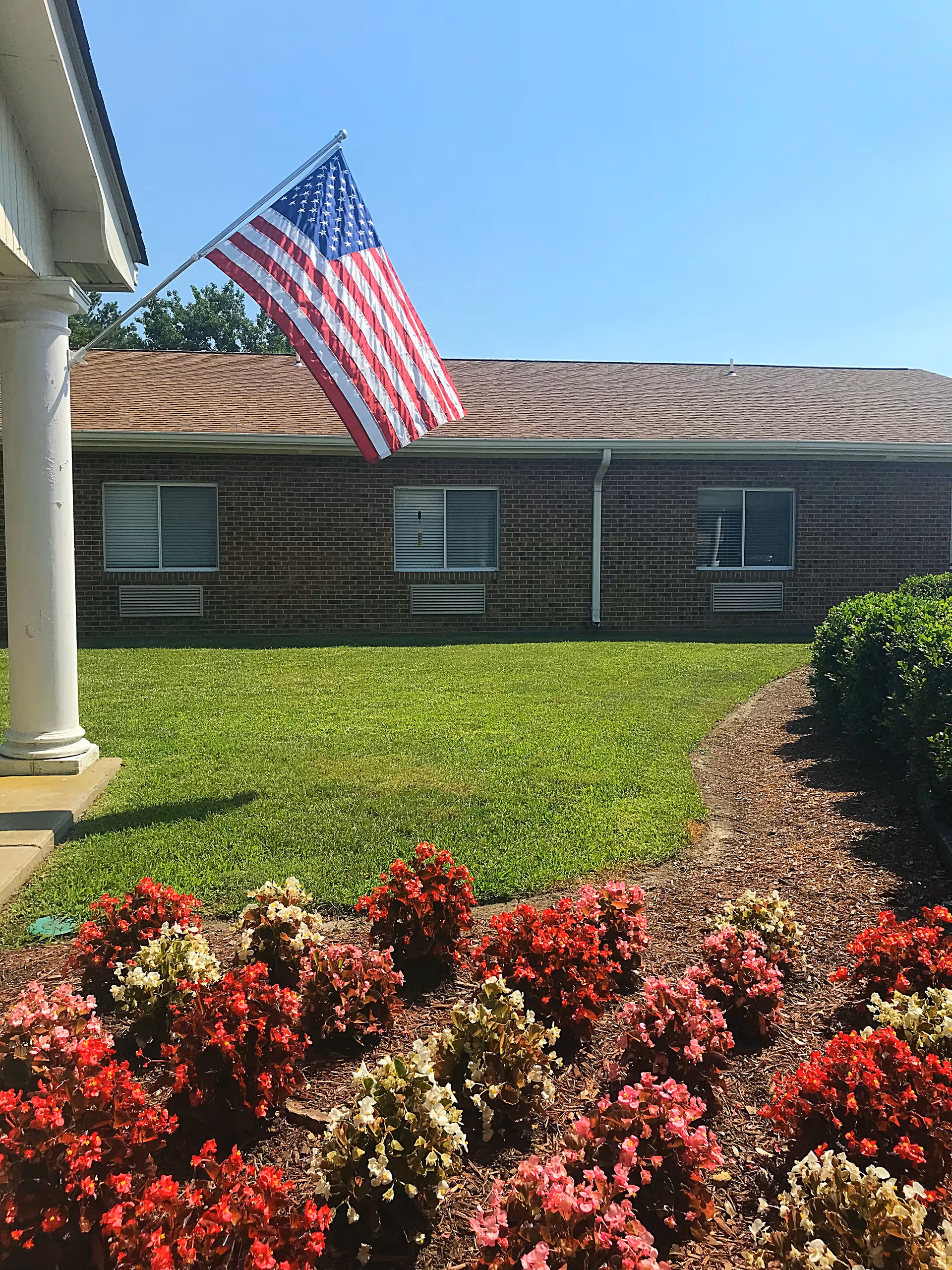 Exterior view of Kempsville Health & Rehab Center with flag, brick building, and flowering bed.