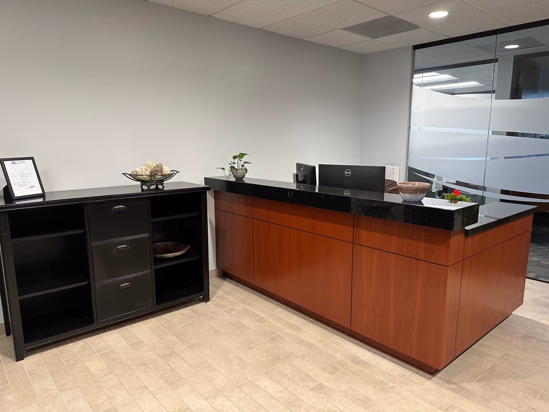 Reception area with wood and black granite counter, plant decor, and glass partition.