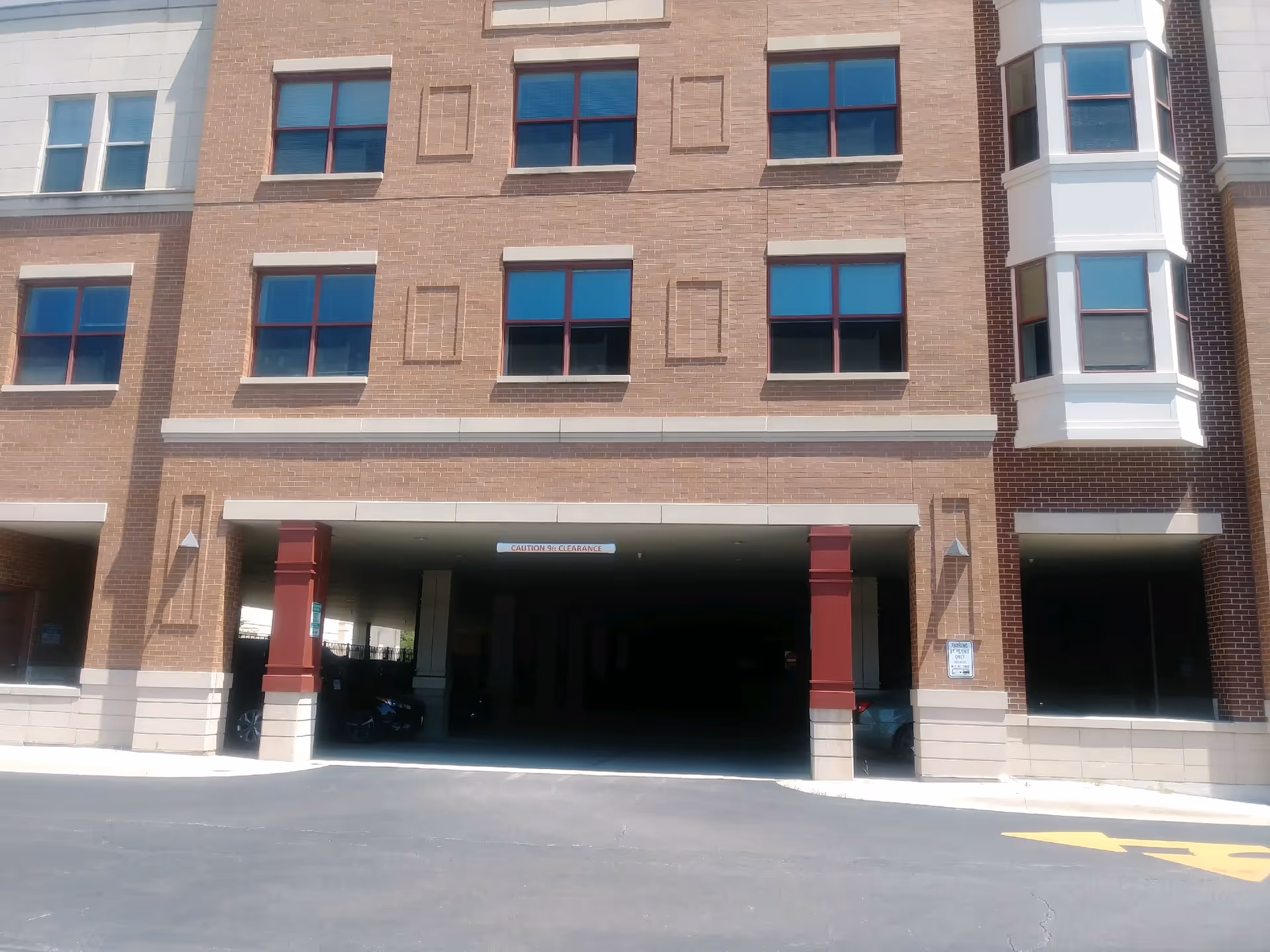 Brick multi-story building with a ground-level parking area and red exterior columns.