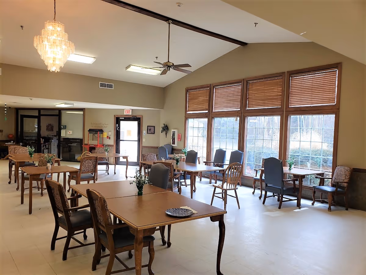 Spacious dining area with wooden tables, chairs, large windows, and a chandelier.
