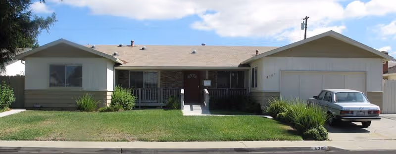 Single-story residential-style senior living facility with a front yard, driveway, and parked car.