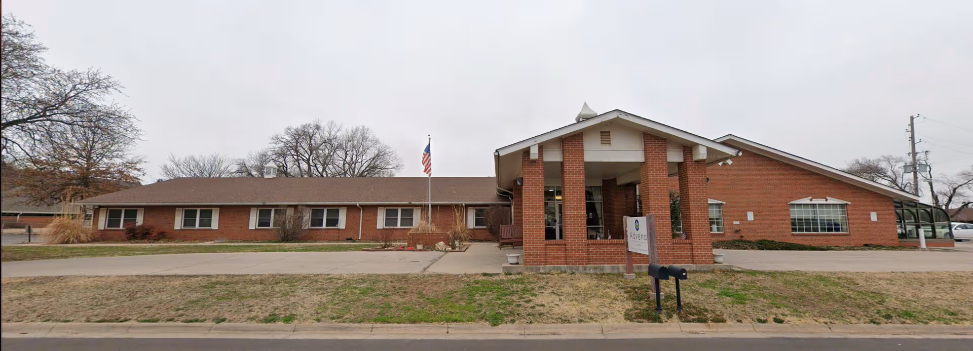 Single-story brick senior living facility exterior with entrance canopy and flagpole.