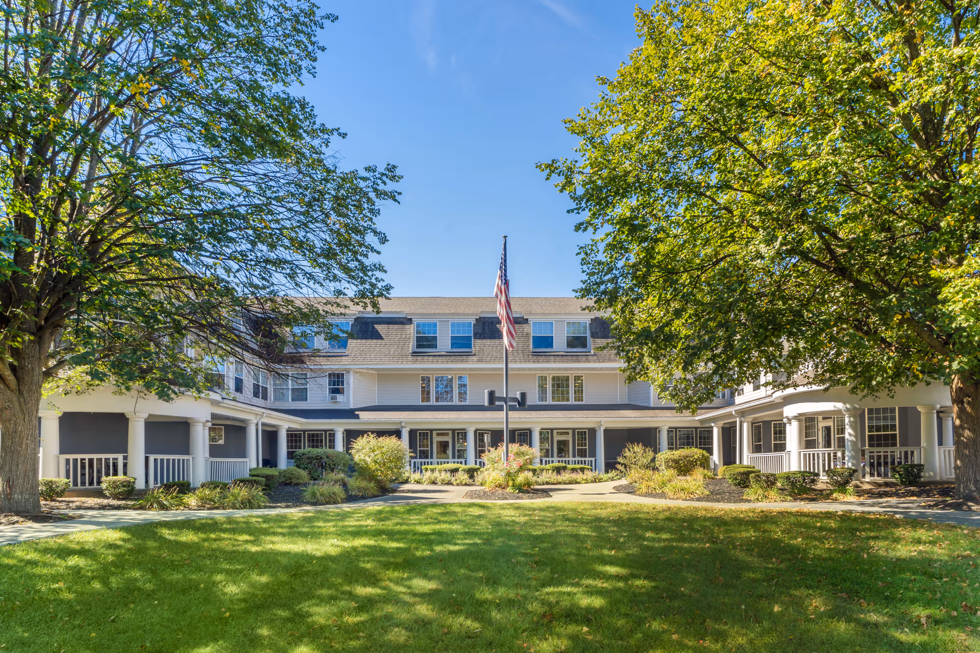 Brookdale Niskayuna senior living building exterior with green lawn, large trees, and a flagpole.
