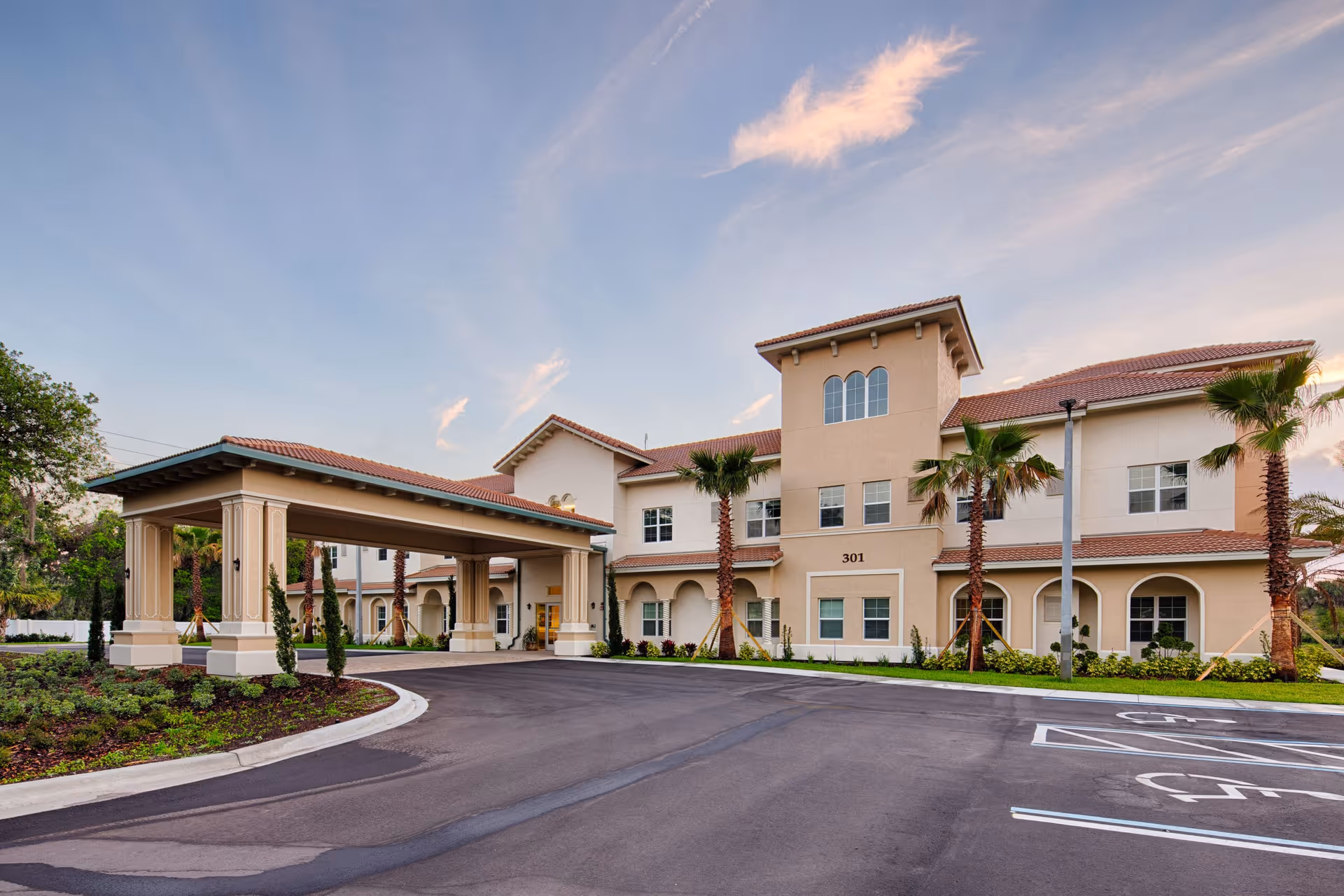 Beige senior living facility exterior with a covered driveway and palm trees.
