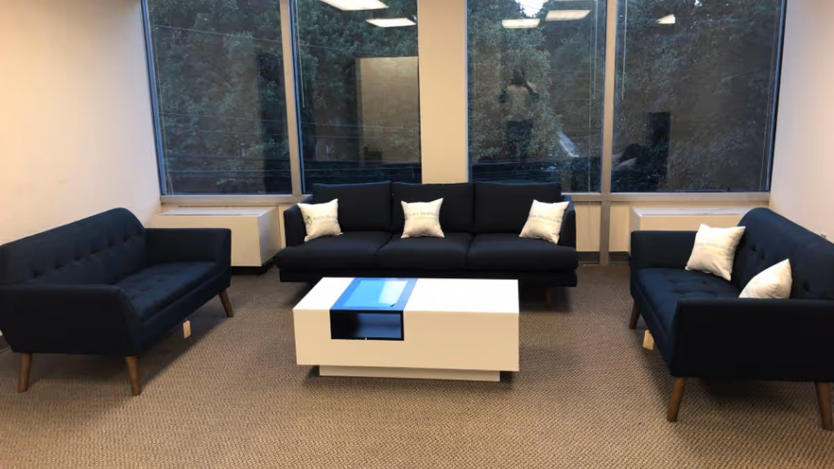 Modern lounge with dark blue sofas surrounding a white coffee table and large windows.