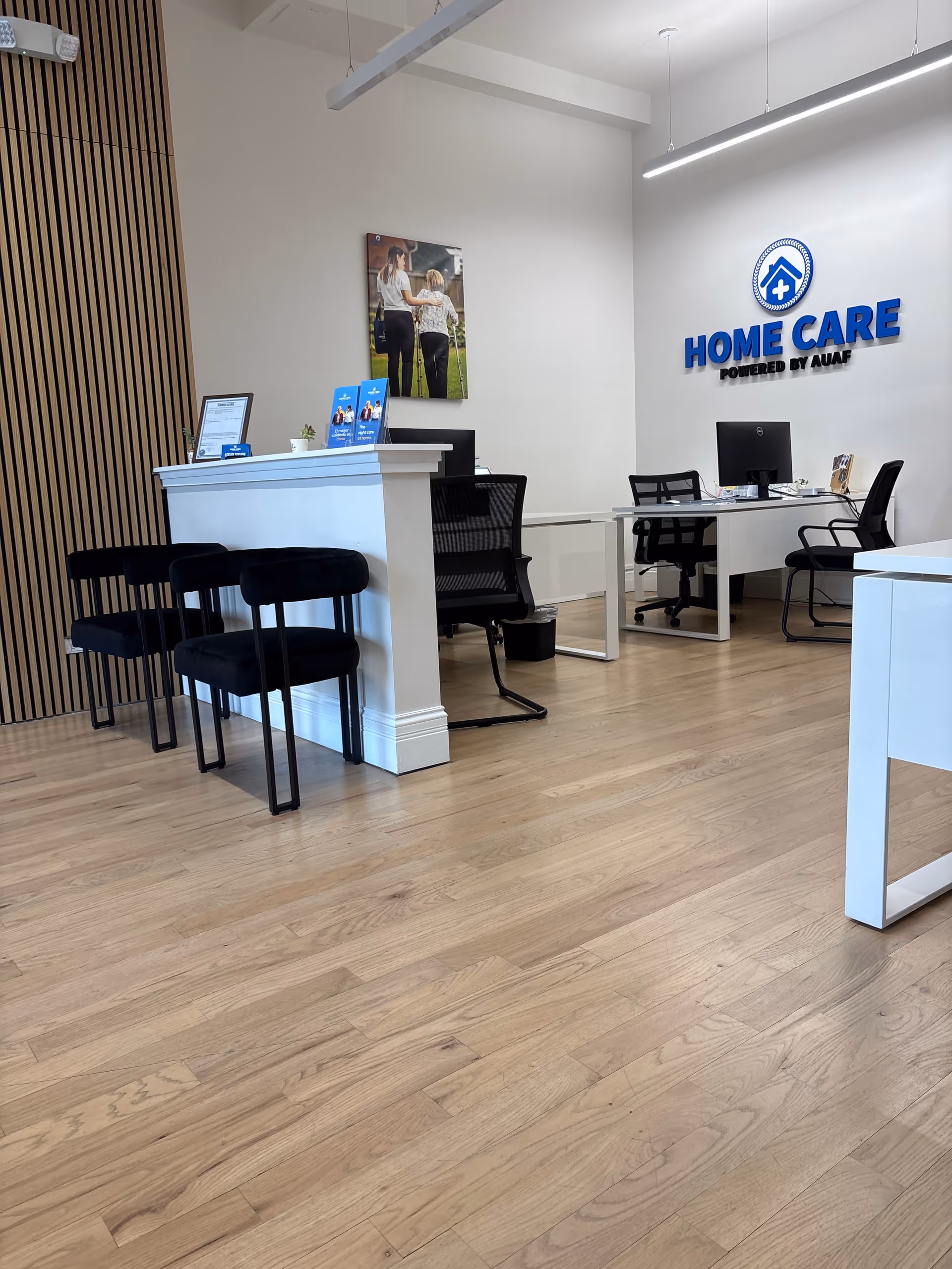 Modern reception area with white desks, black chairs, and a Home Care sign.