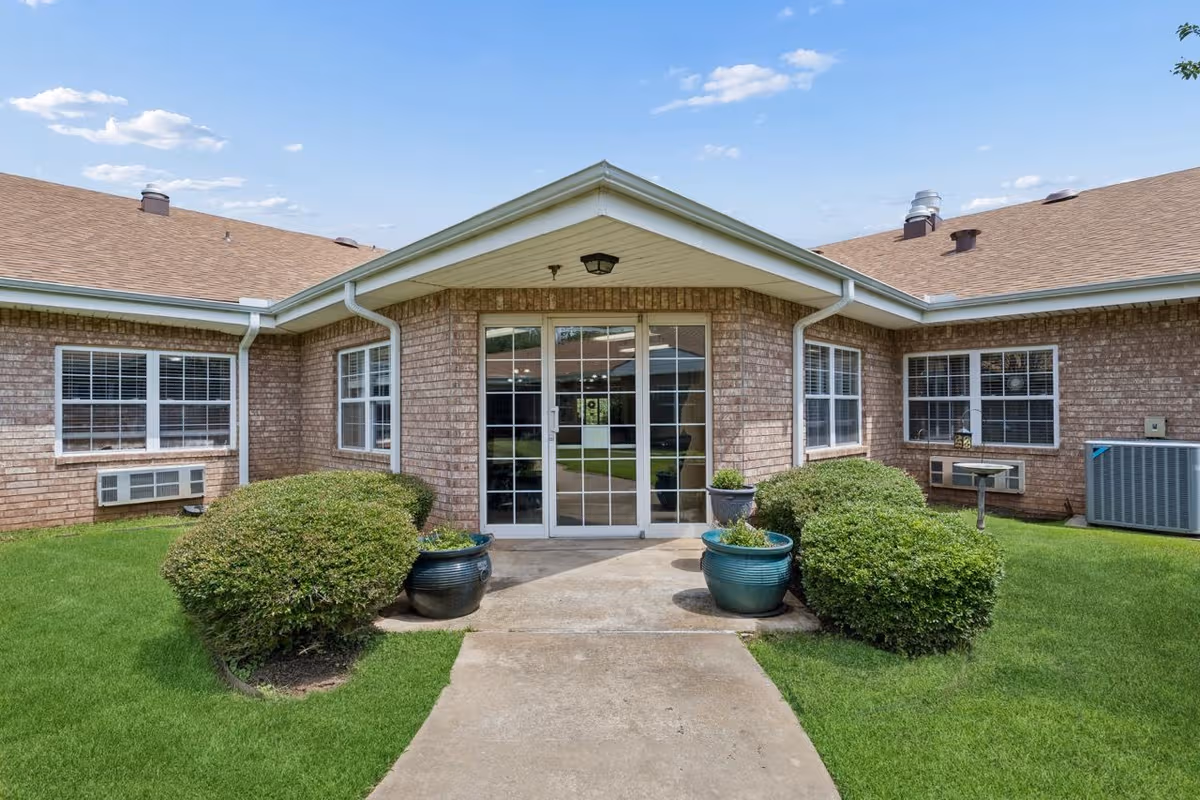 Brick senior living building exterior with glass front doors and manicured shrubs.