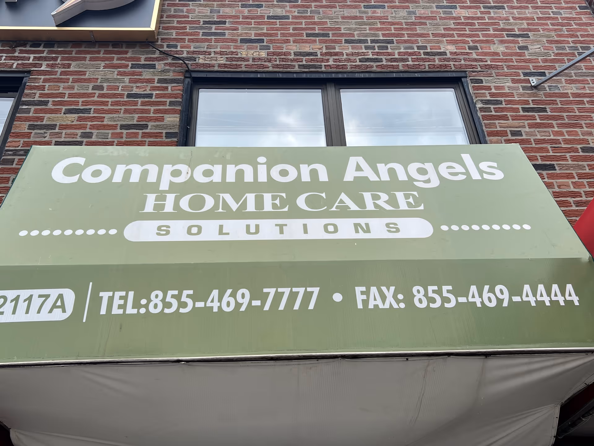 Exterior brick building with a green sign reading Companion Angels Home Care Solutions and contact numbers