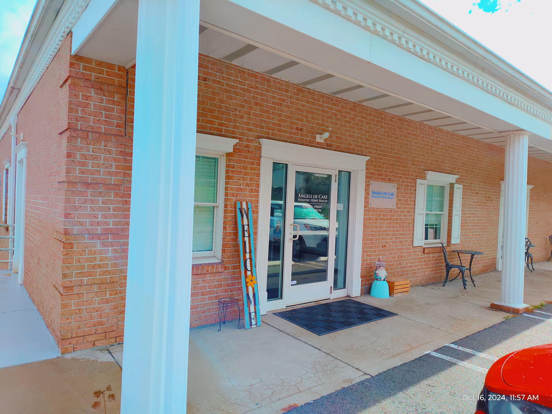 Angels of Care facility entrance with glass doors, signage, brick exterior, and porch seating.
