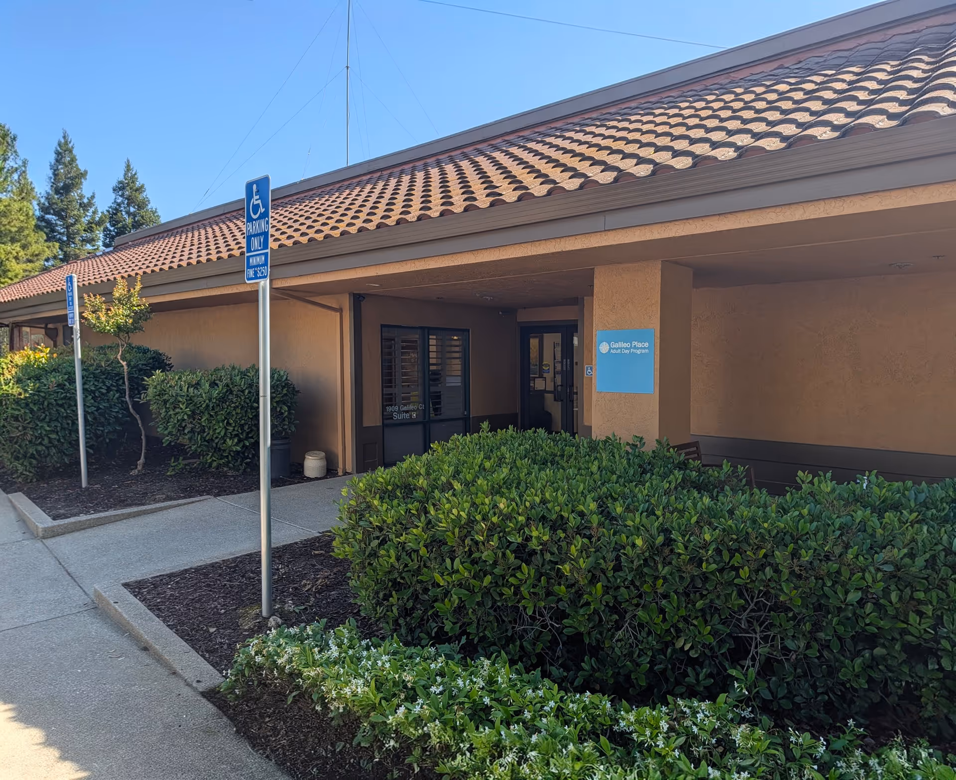 Exterior view of a single-story senior facility entrance with handicap parking and shrubs.