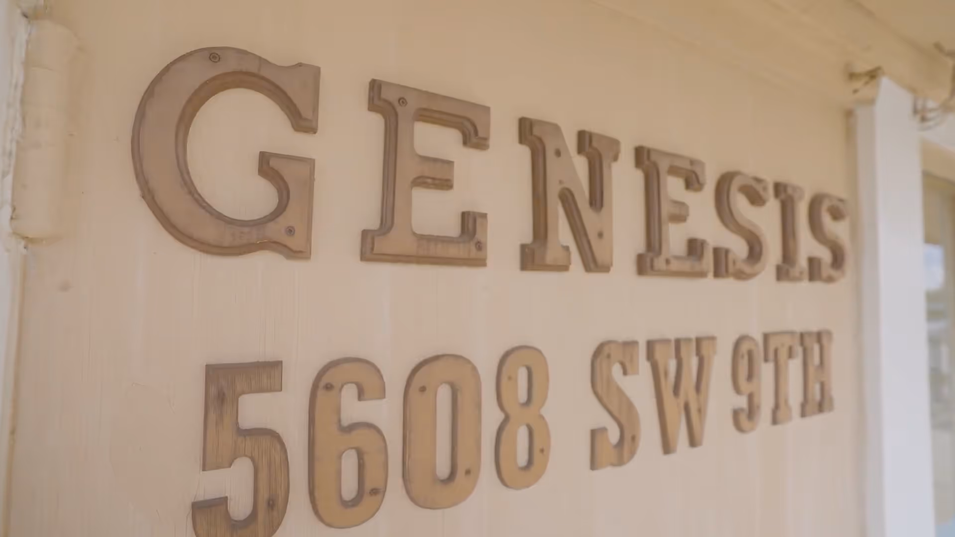 Wooden letters mounted on an exterior wall reading "GENESIS 5608 SW 9TH".