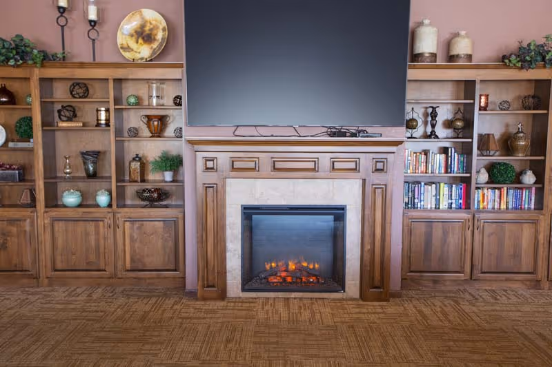 Living room with a wooden fireplace, built-in shelves, and a large mounted television.