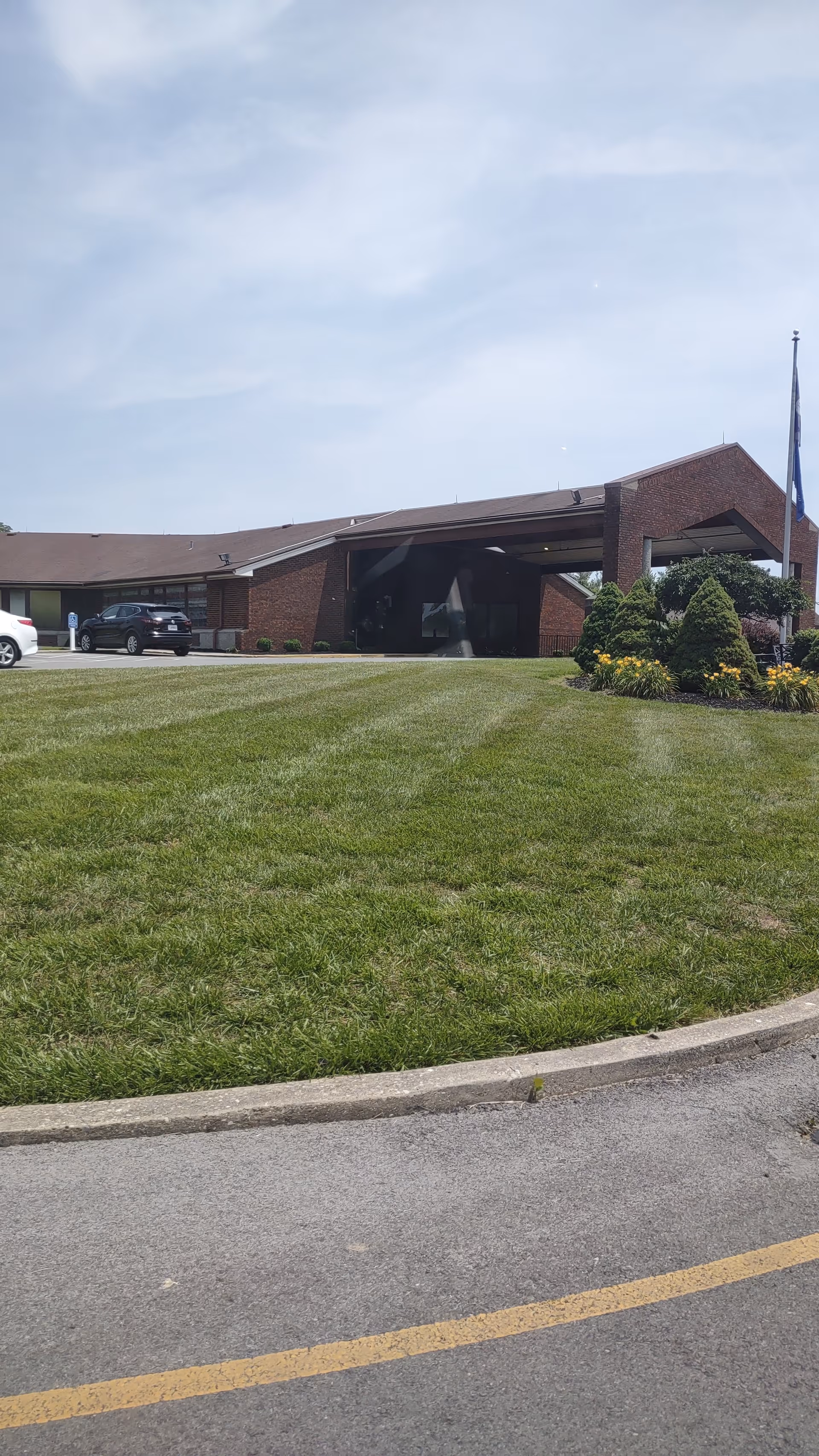 Exterior view of a brick senior living facility with a manicured lawn and driveway.