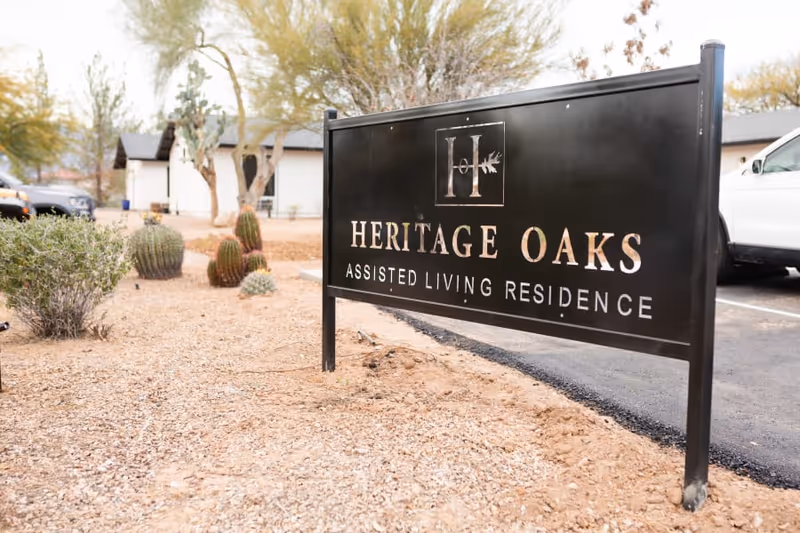 Outdoor sign for Heritage Oaks Assisted Living Residence with desert landscaping and a building in background.