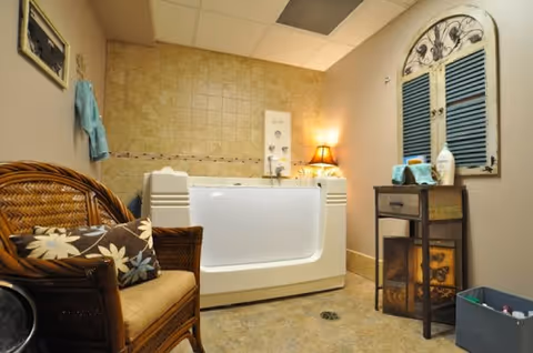 Cozy bathroom featuring a white tub, wicker chair, and small cabinet.