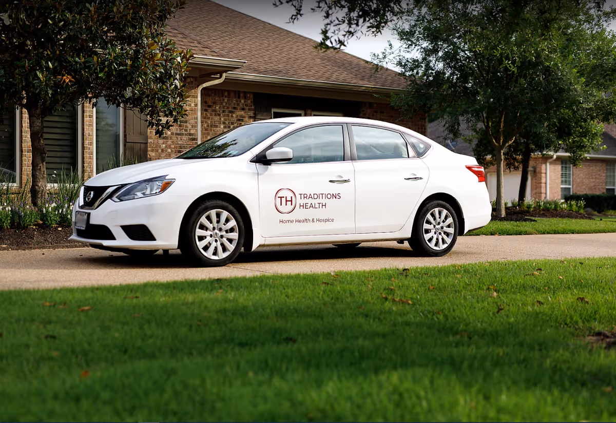 A white sedan with Traditions Health logo parked in front of a brick facility.