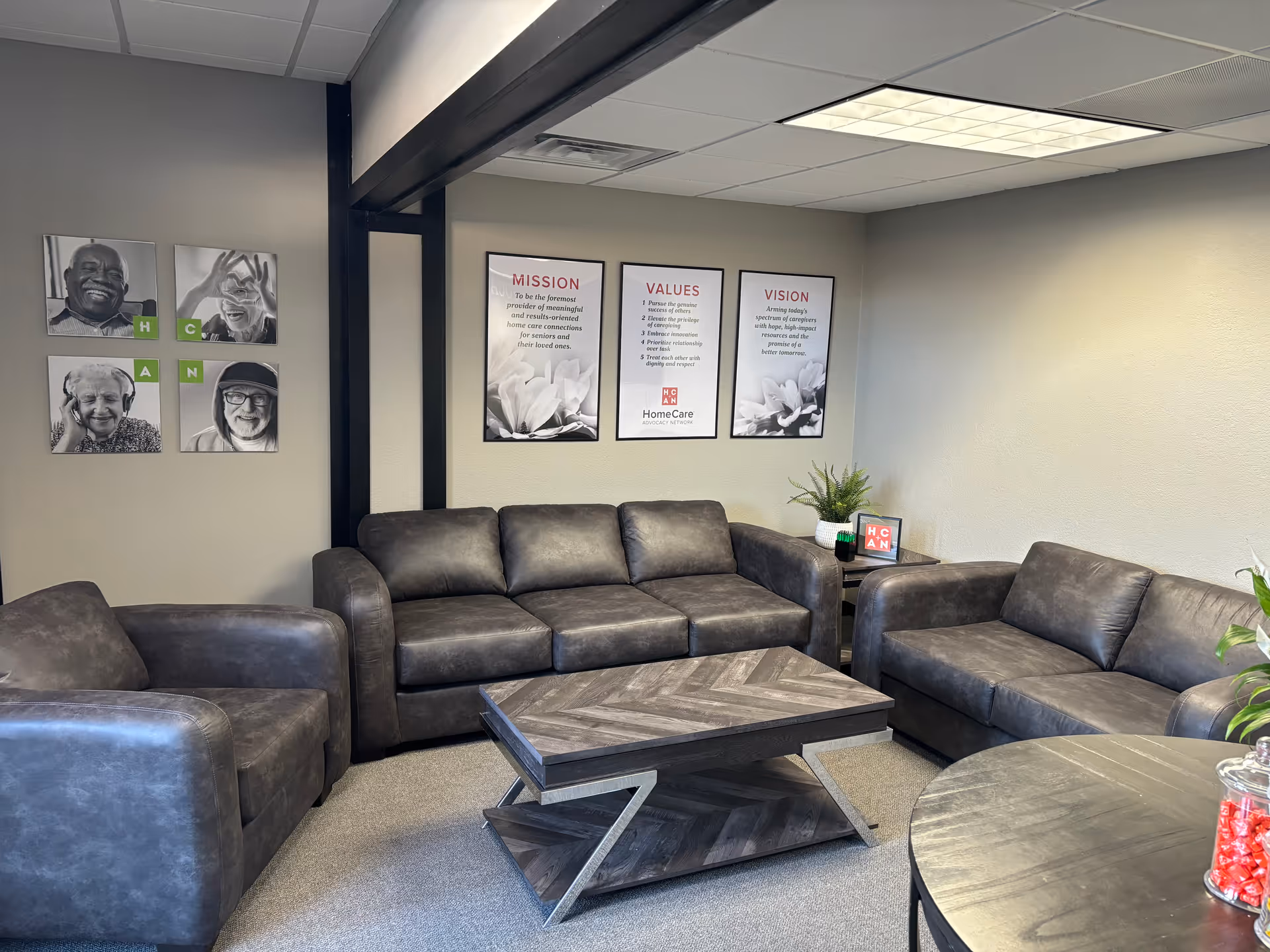 Cozy gray lounge with black leather couches, coffee table, and wall art.