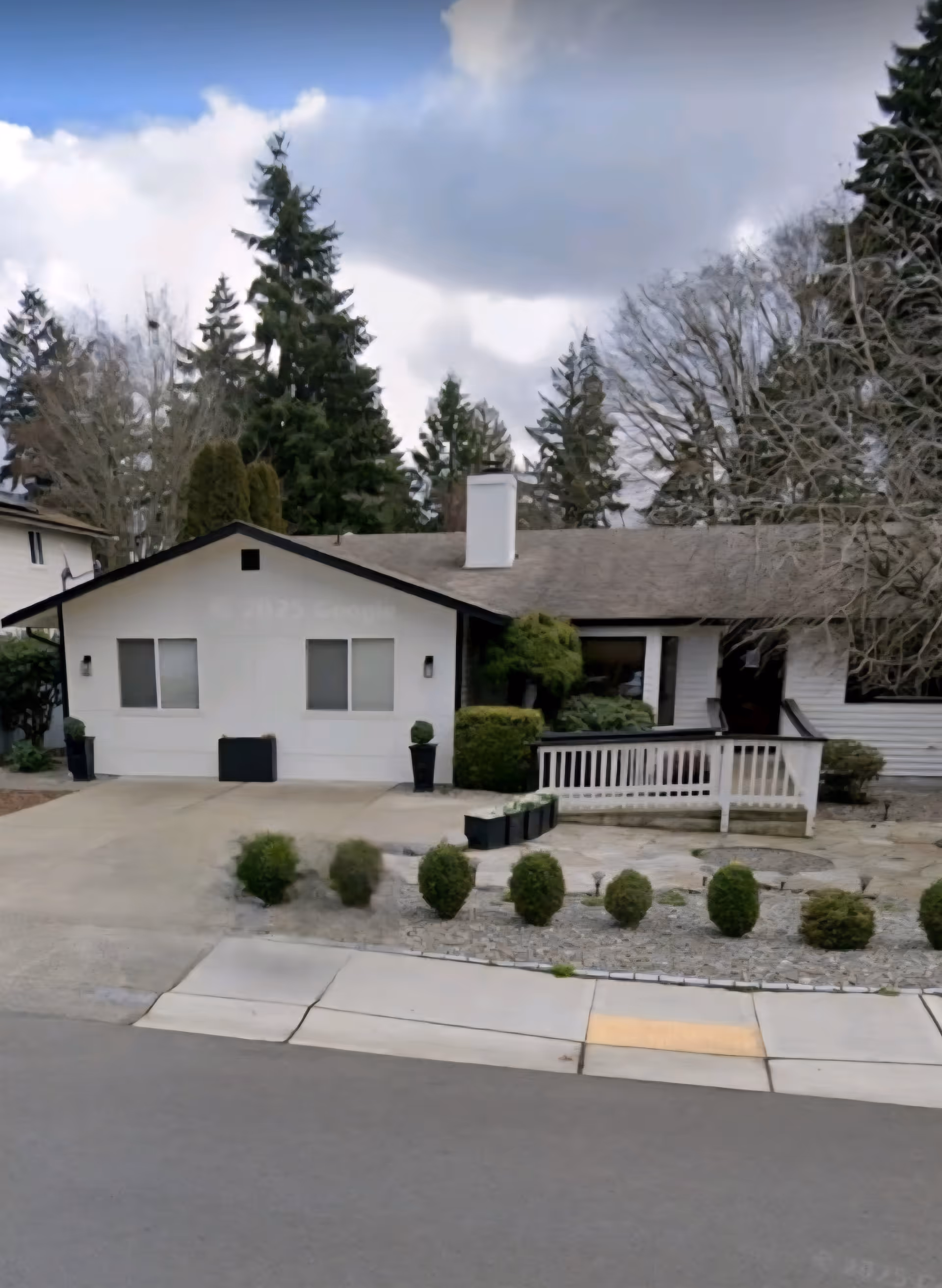 Front view of a single-story white building with a small porch and trimmed shrubs.