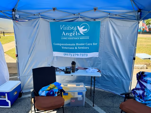 Outdoor tent with Visiting Angels banner, table, cooler, and chairs.