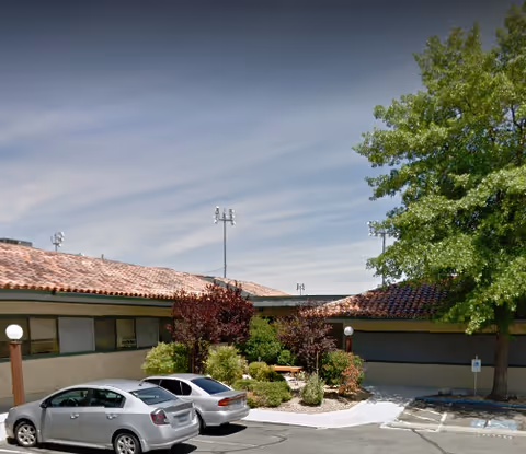 Exterior view of a single-story senior living facility with parked cars and landscaping.