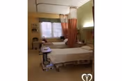 Private patient room with two beds, curtains, and a caregiver attending.