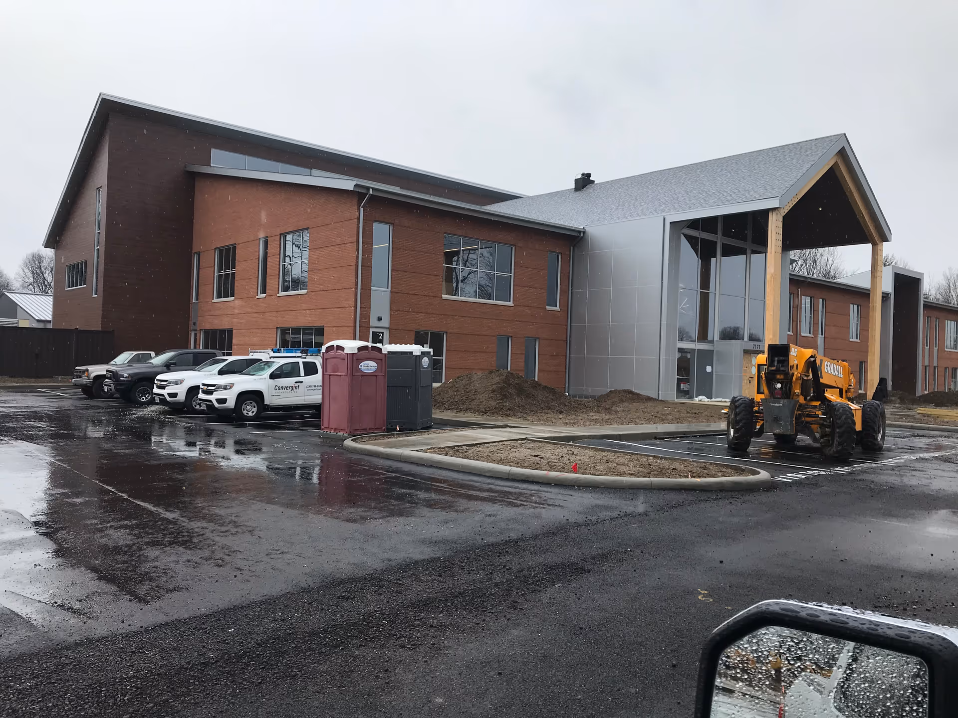 Modern building exterior under construction with equipment, portable toilets, and parked service vehicles.