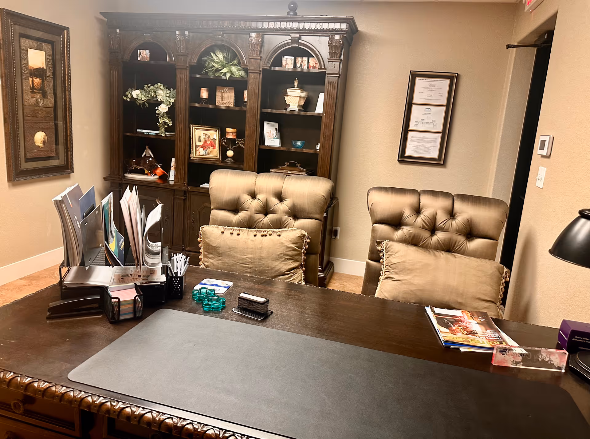A dark wood executive desk with two tufted chairs and a cabinet in a beige office.
