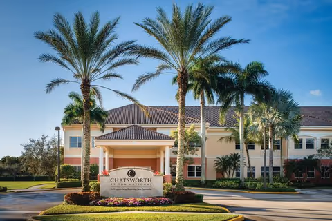 Exterior view of Chatsworth Assisted Living Community at PGA National with palm trees and front sign.