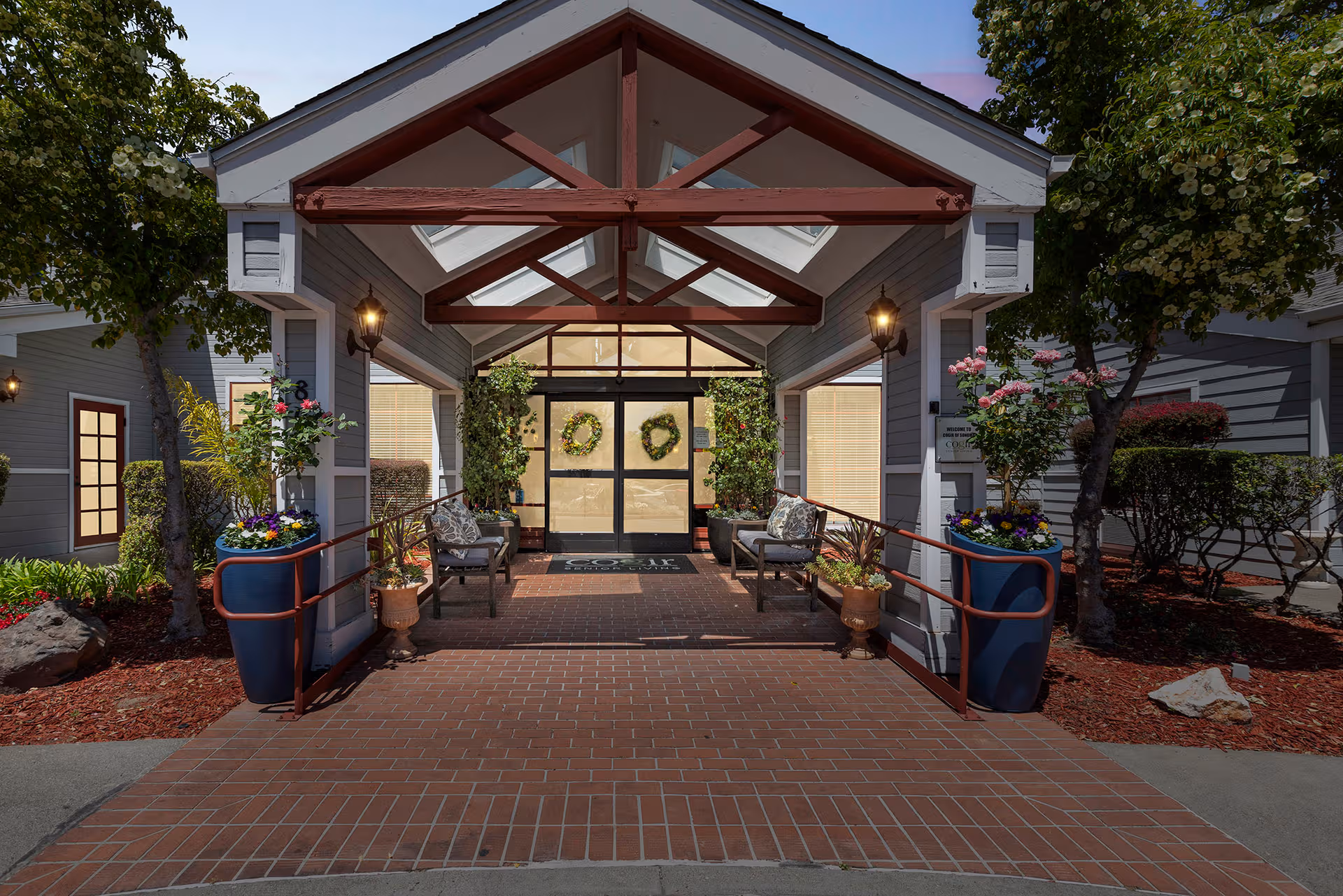 Entrance of Cogir of Sonoma senior living with glass doors, wreaths, benches, and planters.