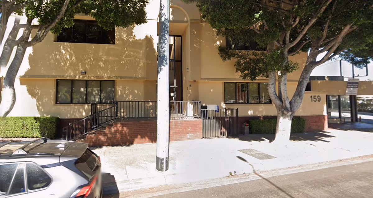 Exterior view of a beige building entrance with stairs and trees.