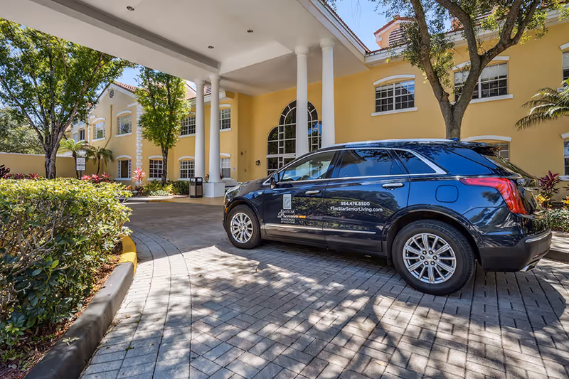 Yellow senior living facility entrance with white columns and a dark blue SUV parked outside.