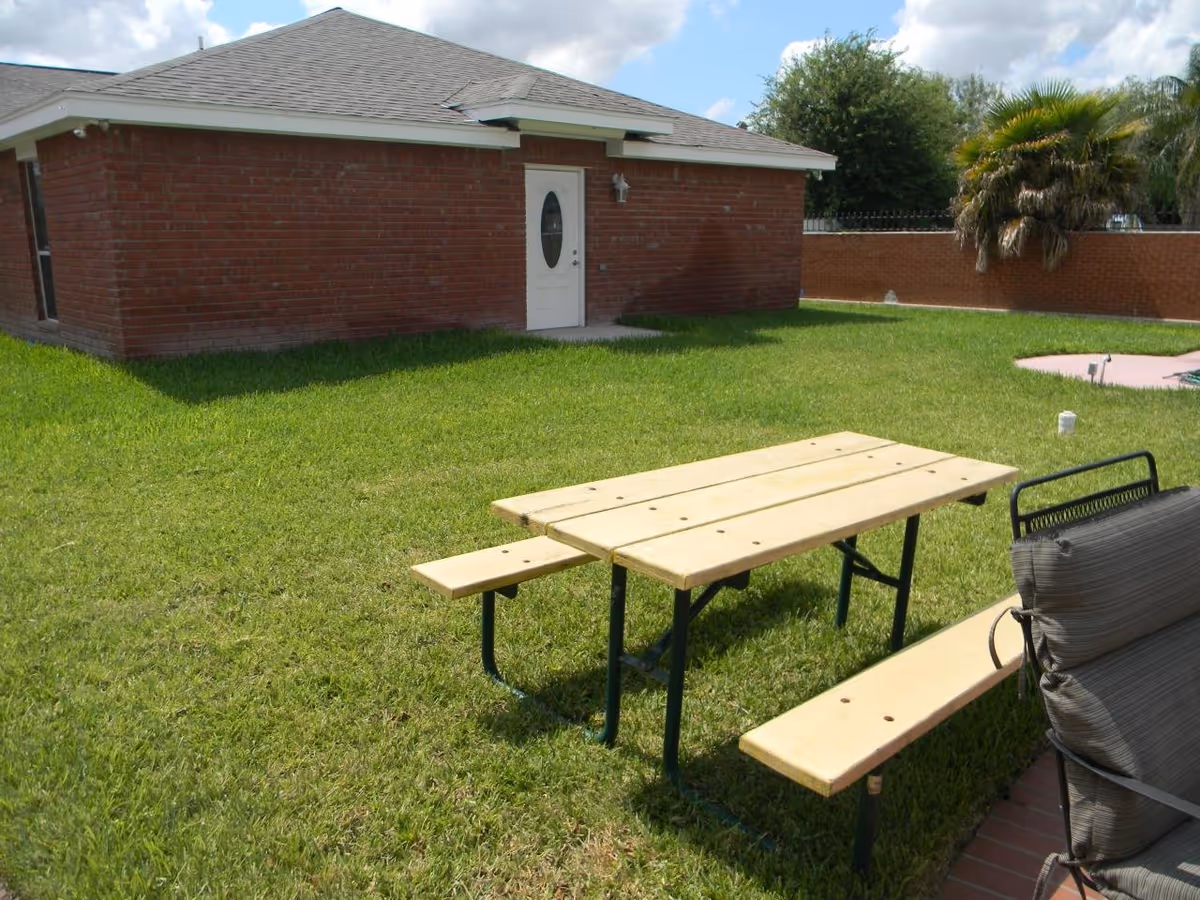 Green lawn with wooden picnic table and brick building, outdoor seating area visible.