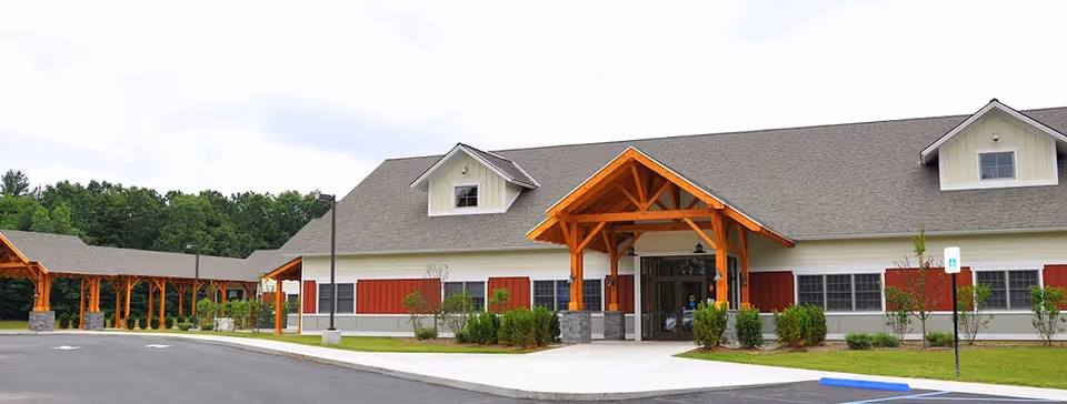 Exterior view of a senior living facility with a wooden entry canopy and red shutters.