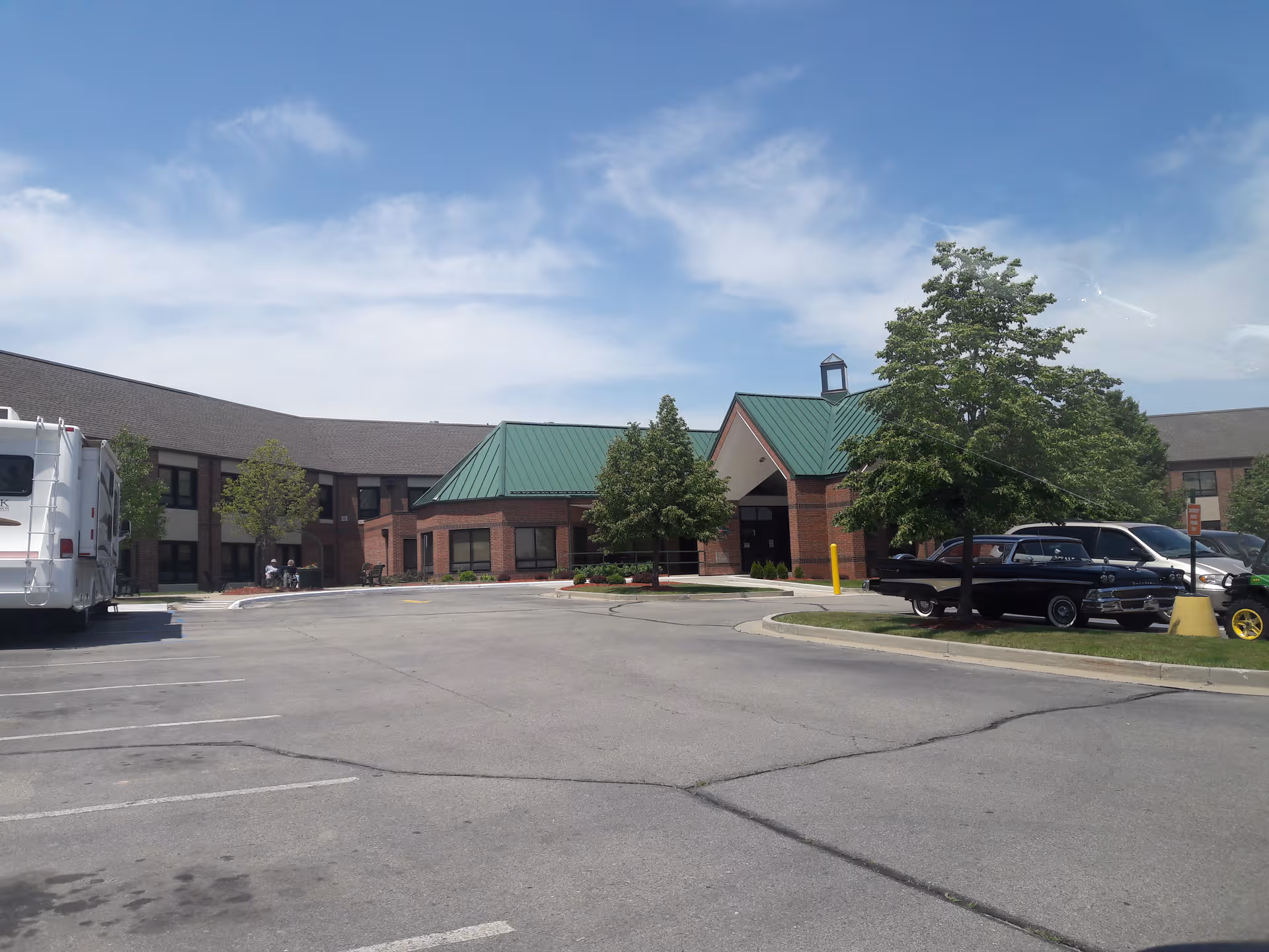 Senior care facility exterior with brick building, green roof, and parked cars.