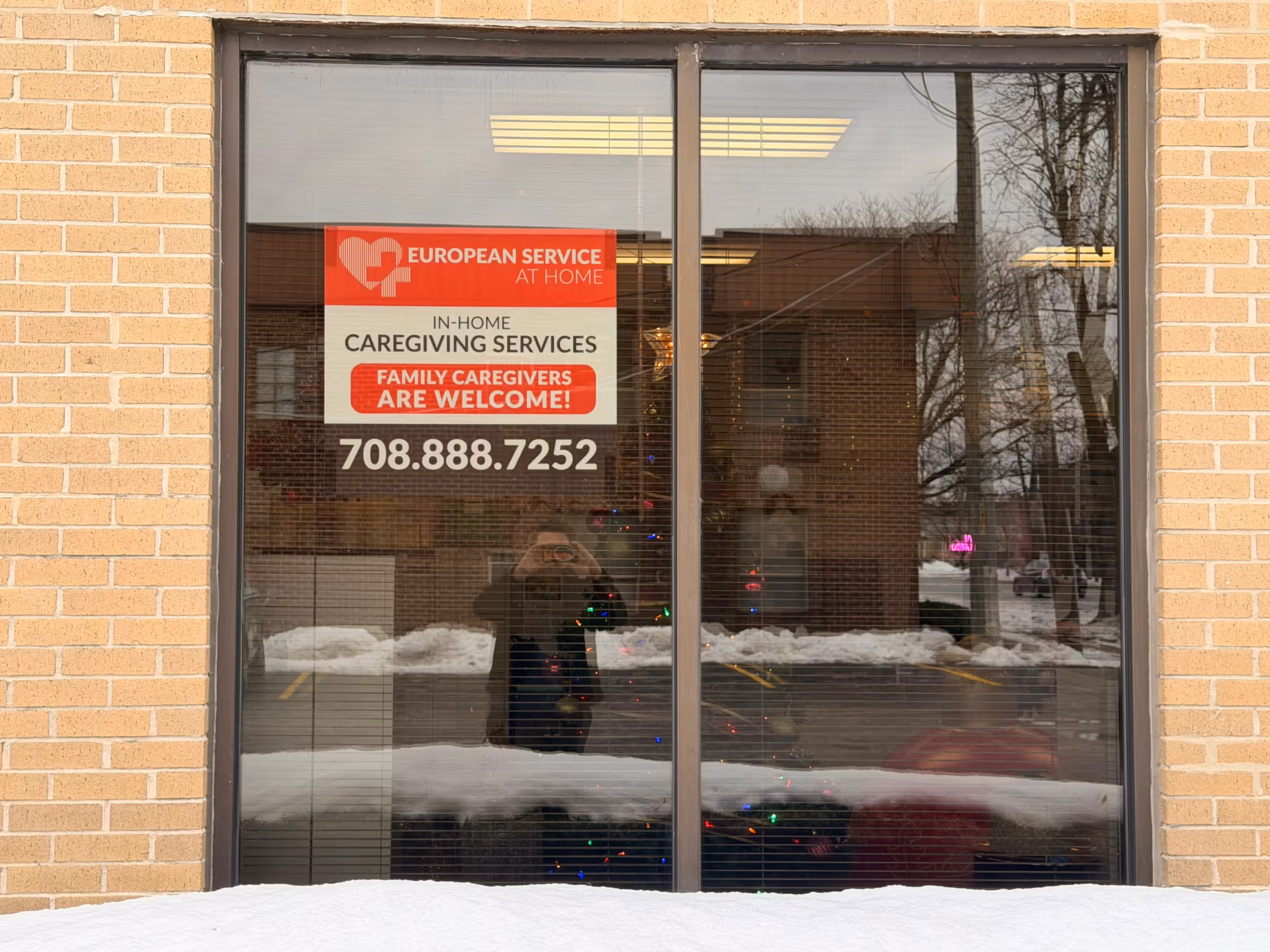Brick building exterior window displays a sign for European Service at Home caregiving with phone number.