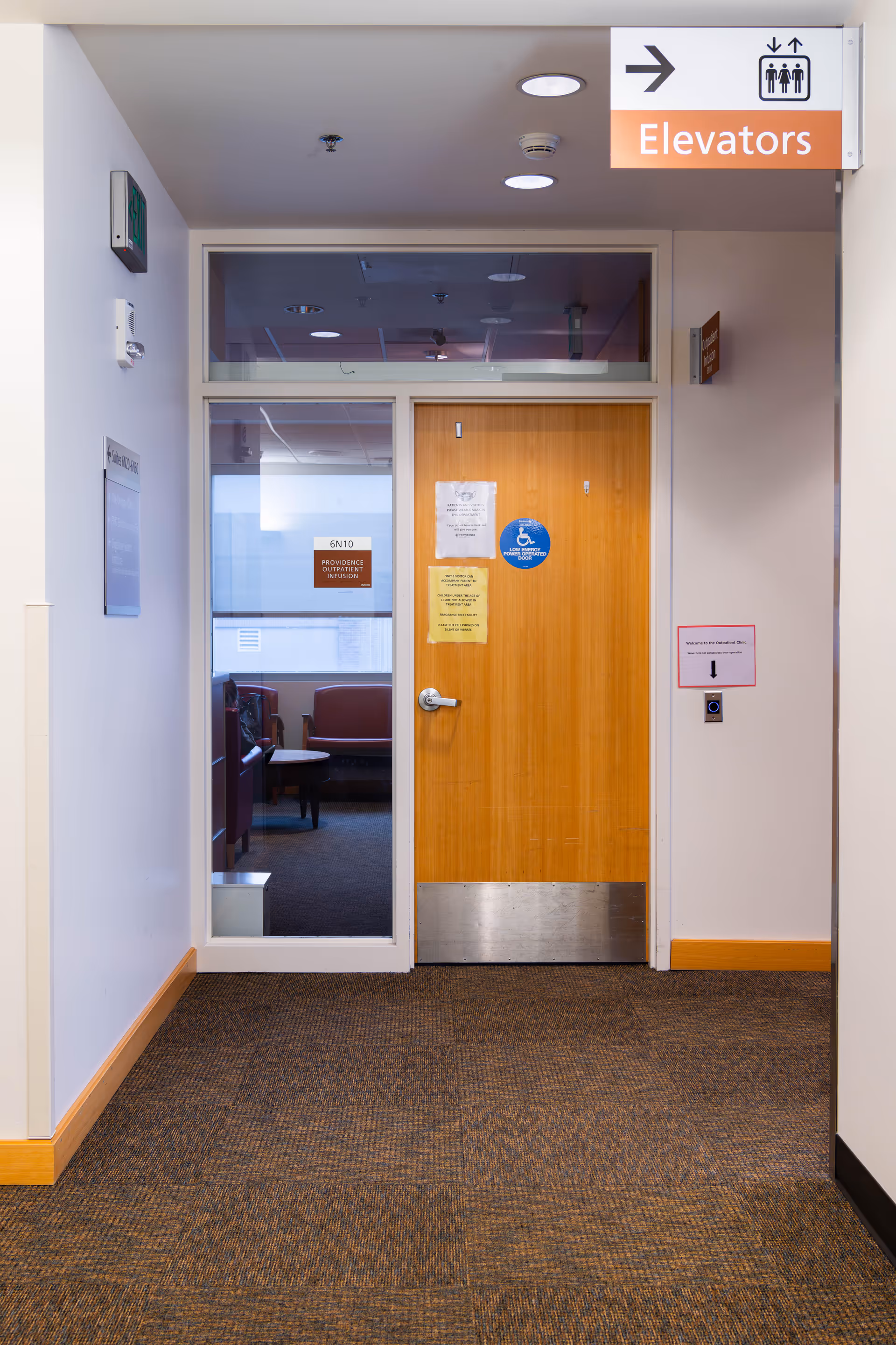 Interior hallway with a wooden door, glass panels, and an elevators sign overhead.