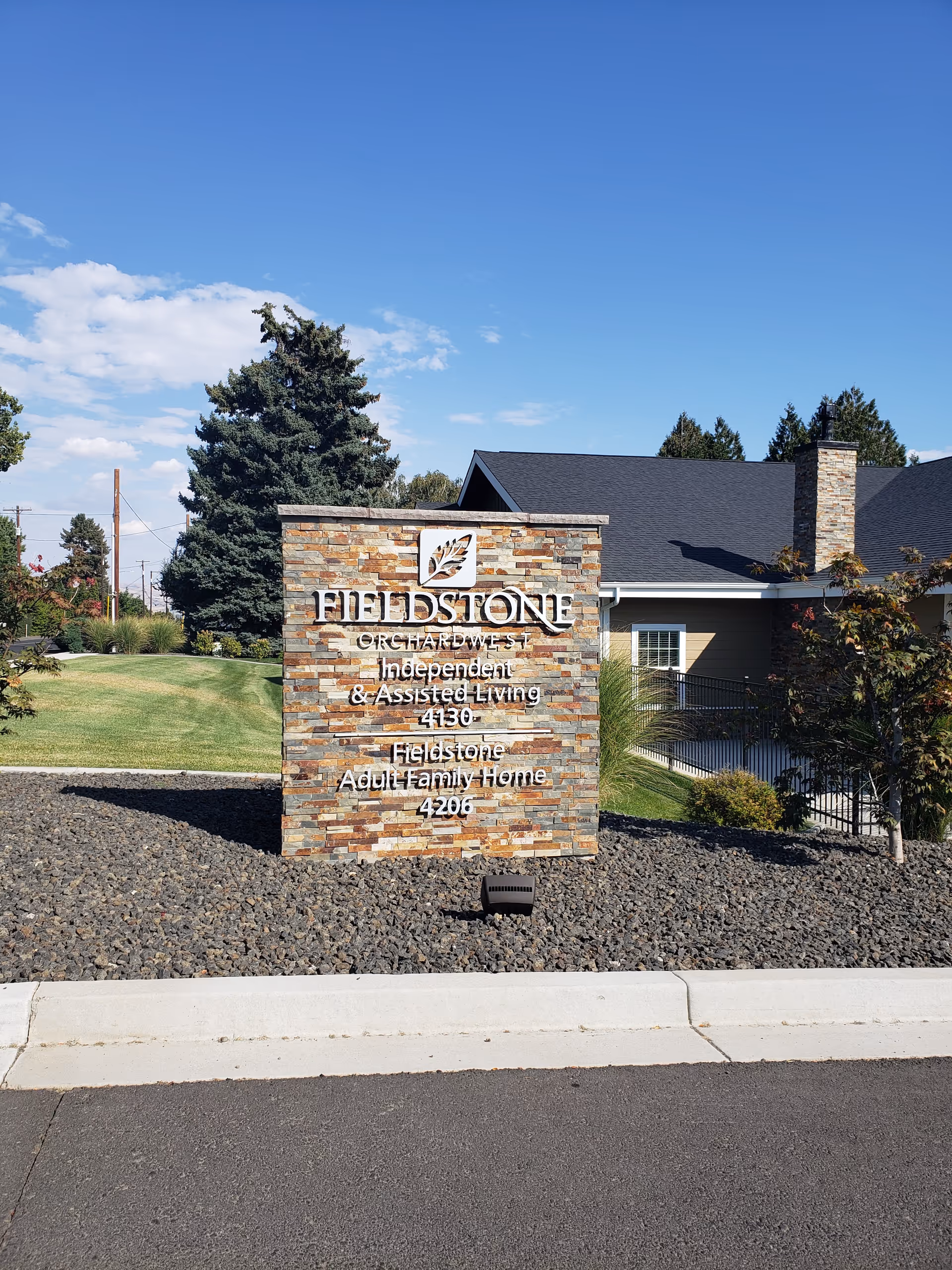 Stone sign with Fieldstone branding stands at the front, amid landscaping and a modern building.