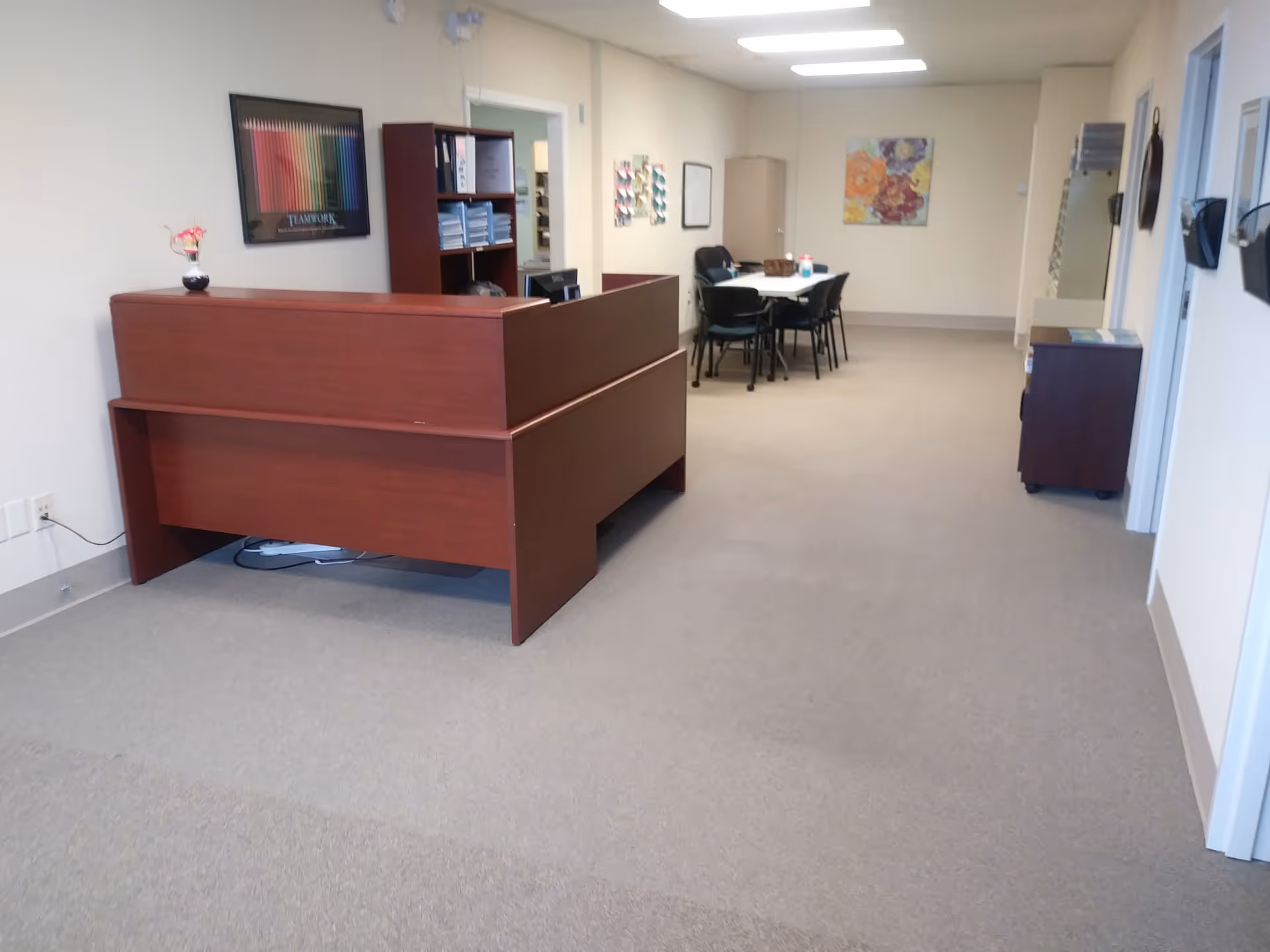 Reception desk in a spacious corridor with a round dining table and chairs visible.