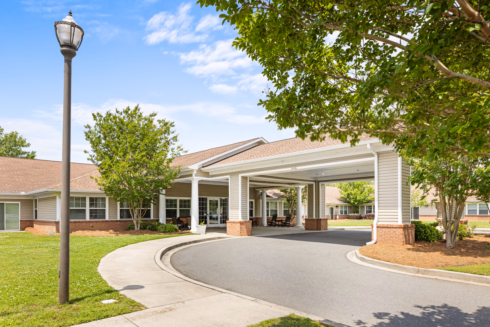 Exterior view of TerraBella Rock Hill facility entrance with a covered drop-off area, surrounded by green trees and a clear blue sky.