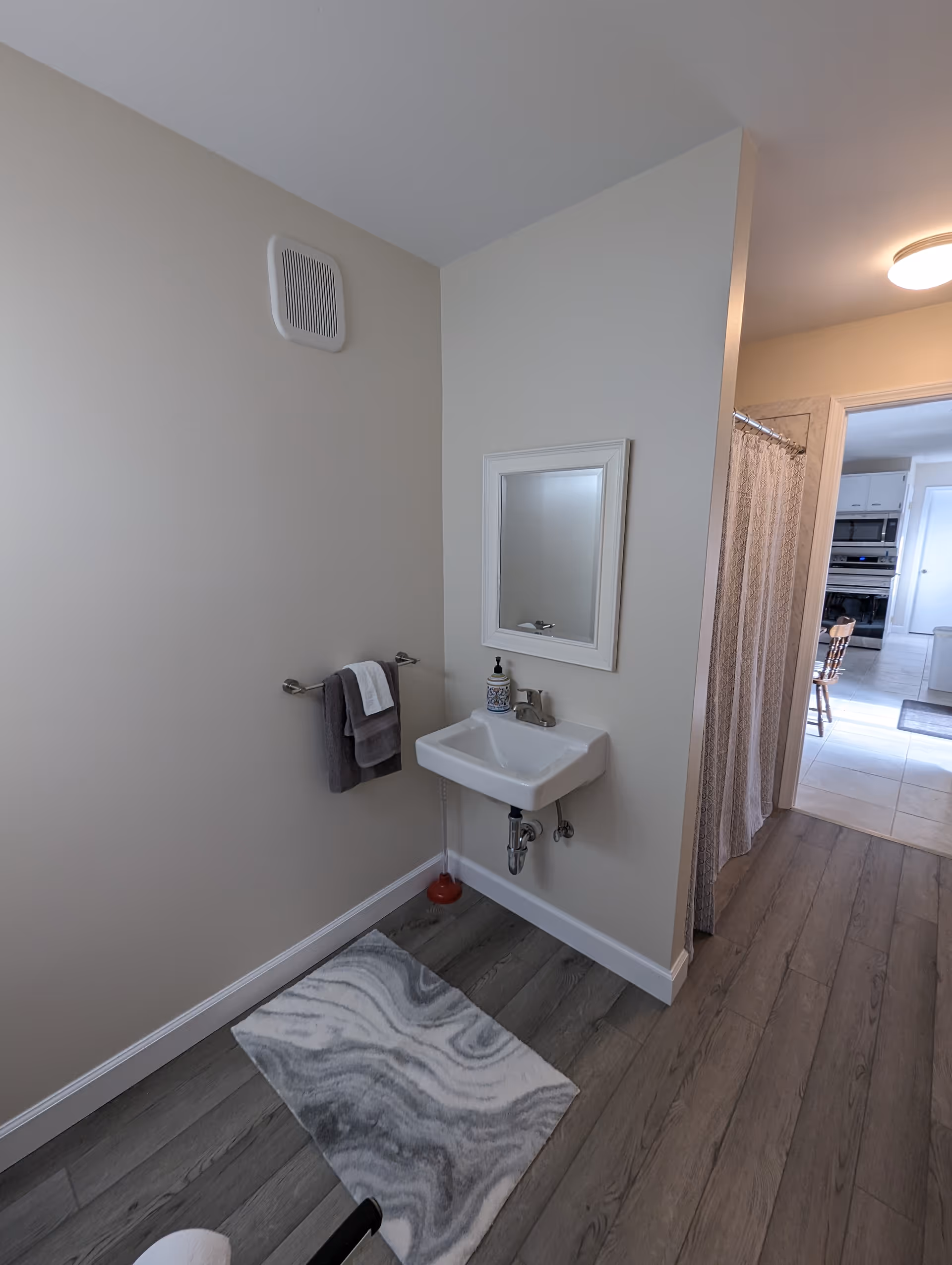 Small bathroom featuring wall sink, mirror, towel bar, rug, and doorway to kitchen