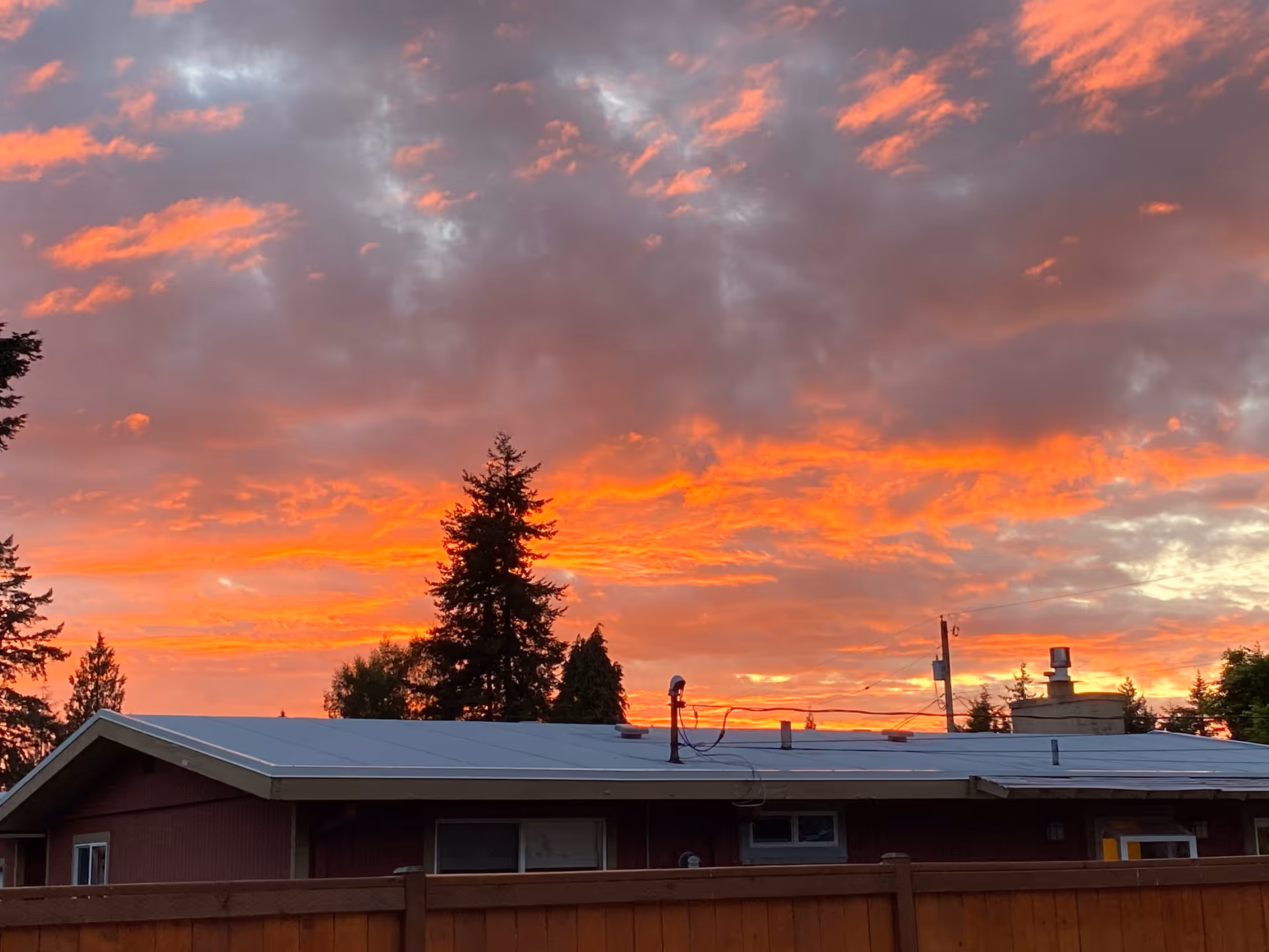 Sunset sky over a single-story building with a wooden fence in front.