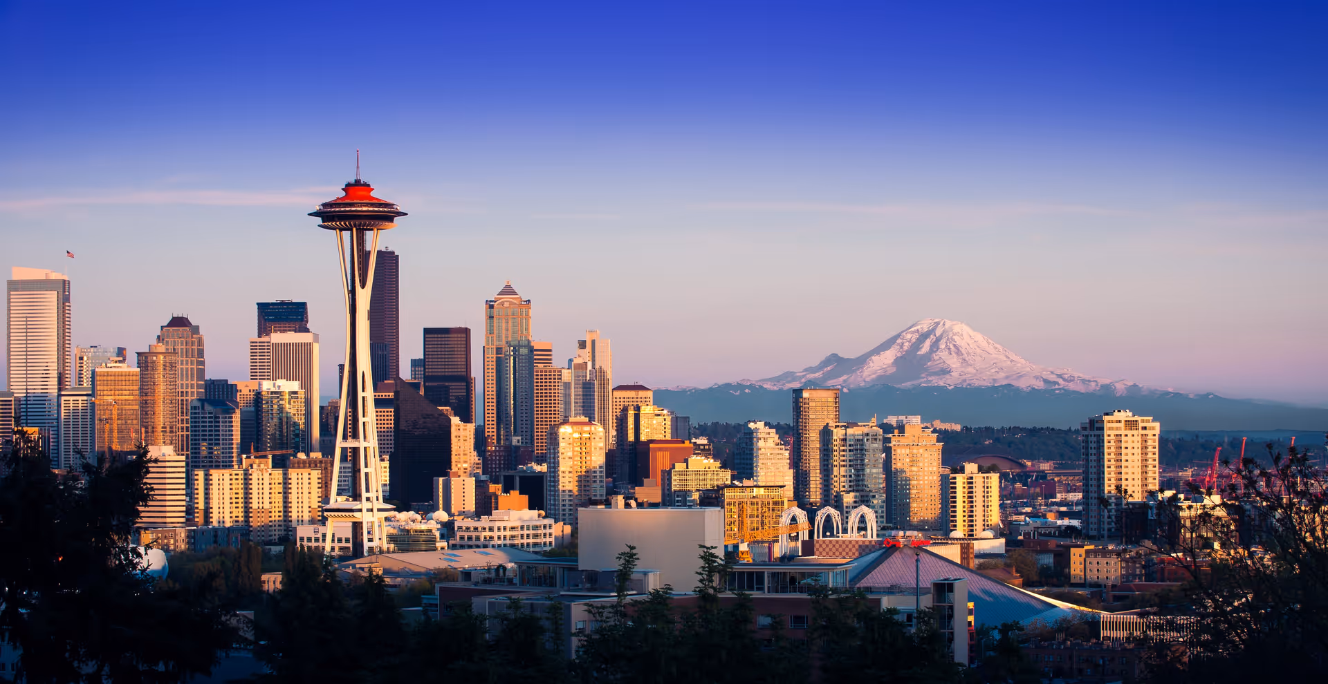 Seattle skyline featuring the Space Needle with Mount Rainier in the background at sunset.
