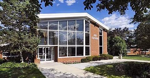 Brick senior living facility with a glass-front entrance and surrounding trees.