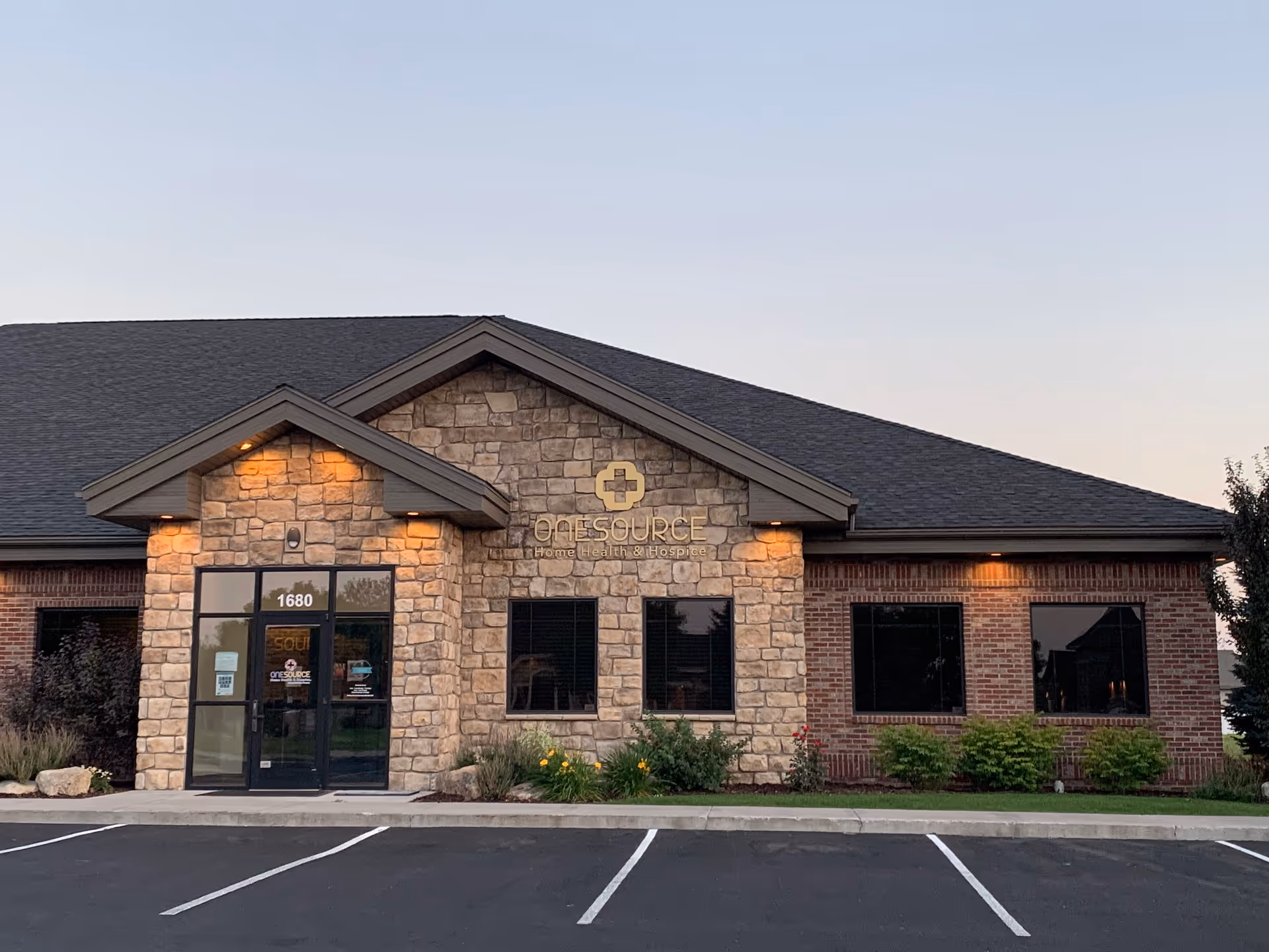 Stone and brick facility front with OneSource sign, glass entry doors, and a parking lot.